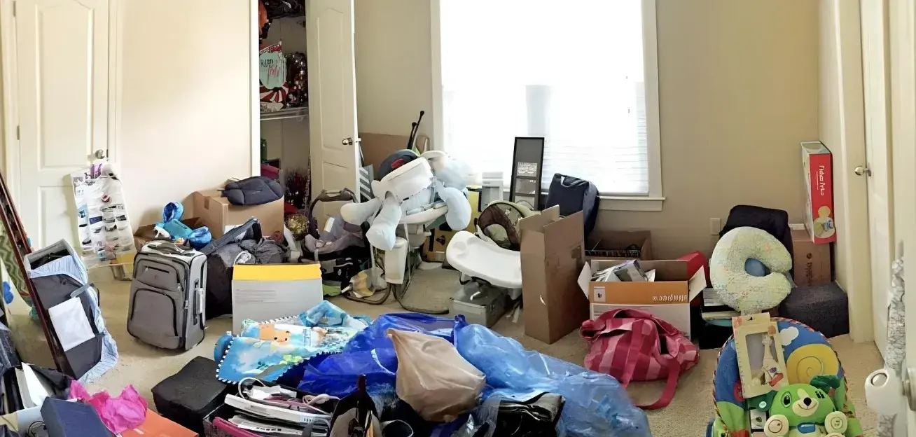 Nursery before: floor covered in moving boxes, luggage, and loose baby gear, closet door blocked by clutter.